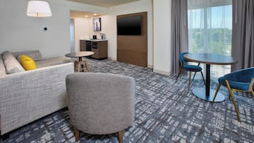 A hotel room with a sofa, armchair, small table, and a TV mounted on the wall.