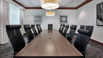 A conference room with a long table and multiple chairs, framed artwork on the walls, and a ceiling light fixture.
