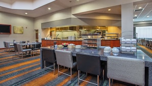 A hotel dining area with a buffet setup, seating arrangements, and a kitchen in the background. - Holiday Inn University Plaza-Bowling Green by IHG (Bowling Green)