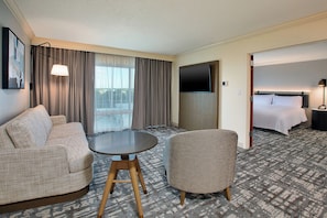 Habitación de hotel con sofá, sillón, mesa redonda, televisión y cama.