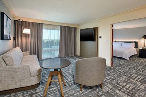 Habitación de hotel con sofá, sillón, mesa redonda, televisión y cama.