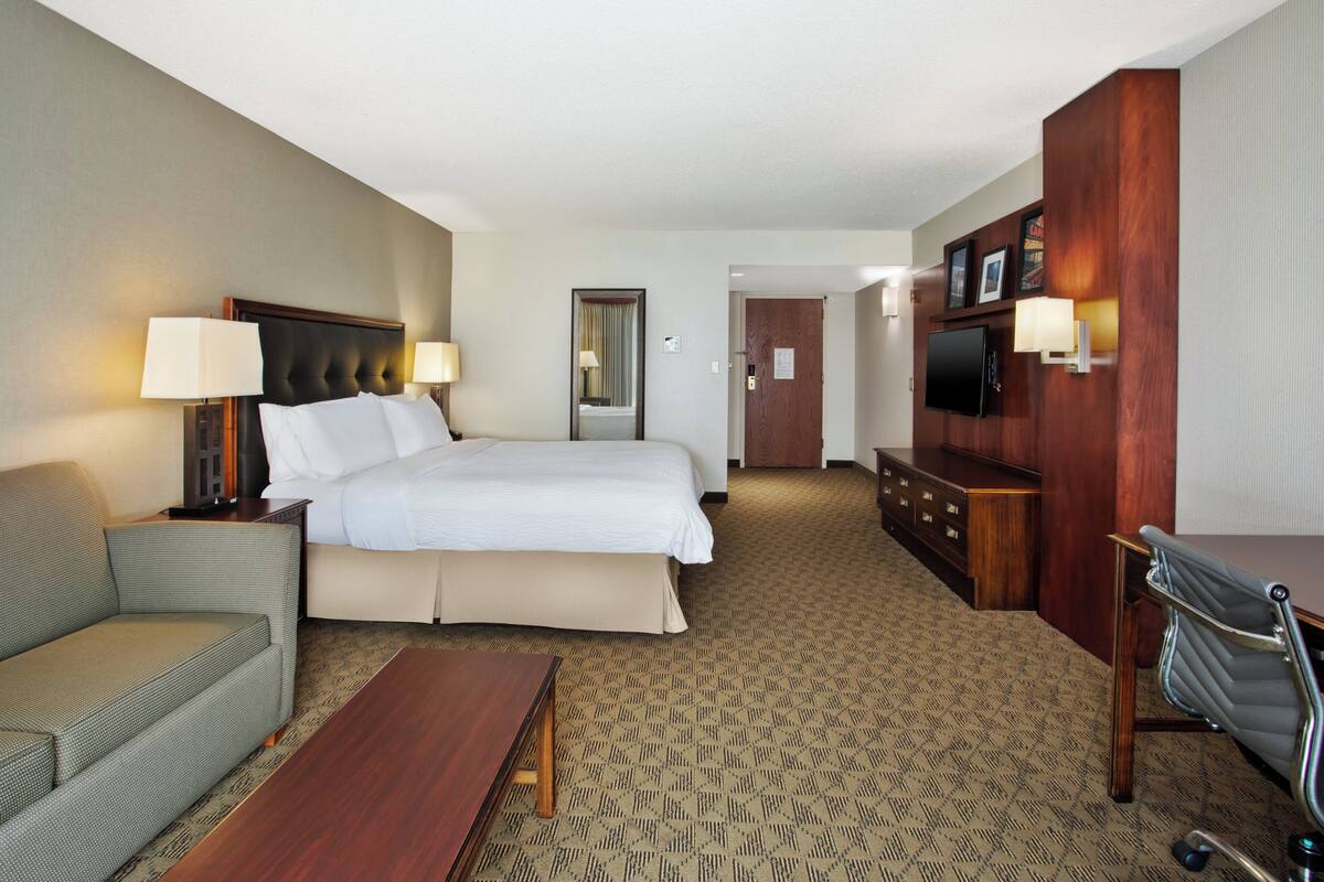 A hotel room with a bed, a sofa, a desk, a TV, and a mirror.