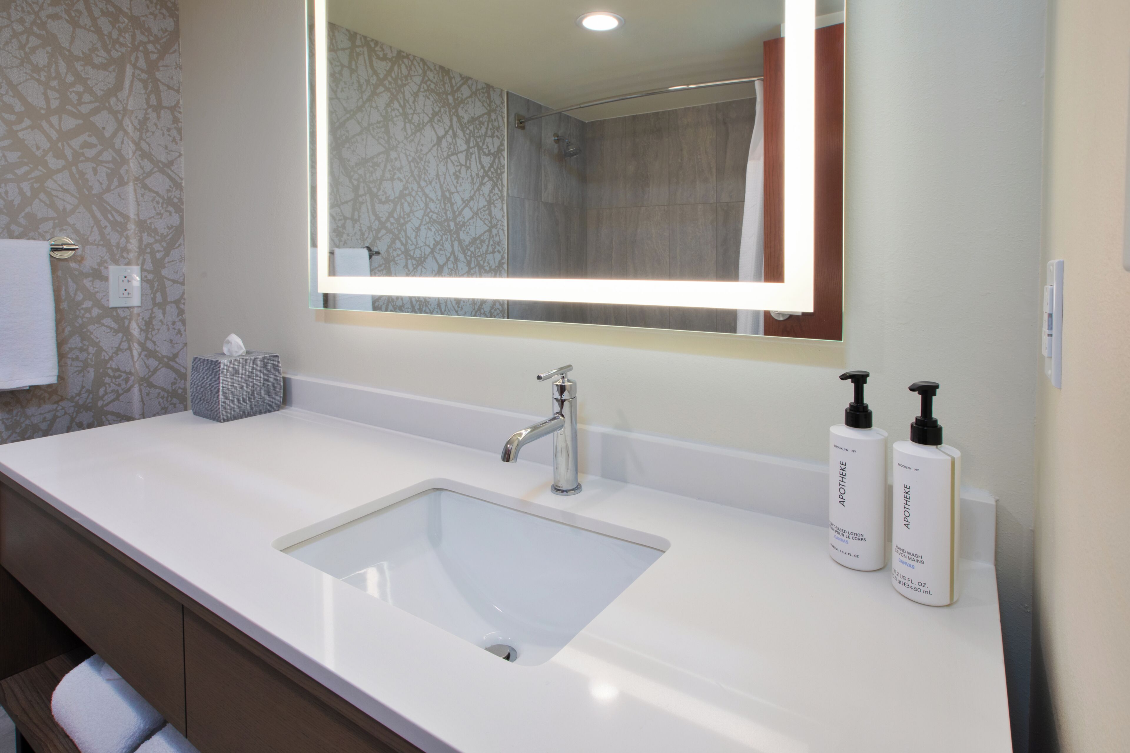 A bathroom with a white sink, a mirror, and two bottles of lotion.