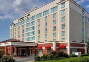 A multi-story hotel with a clear entrance, a covered area with red umbrellas, and a sign reading 'CROWNE PLAZA'.