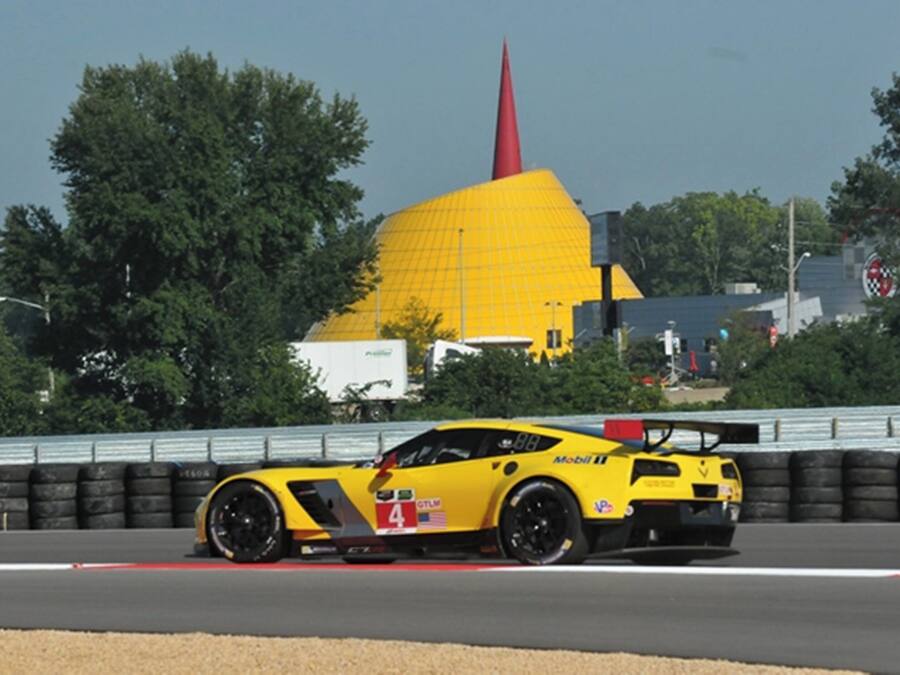 A yellow sports car on a race track with a large yellow building in the background.
