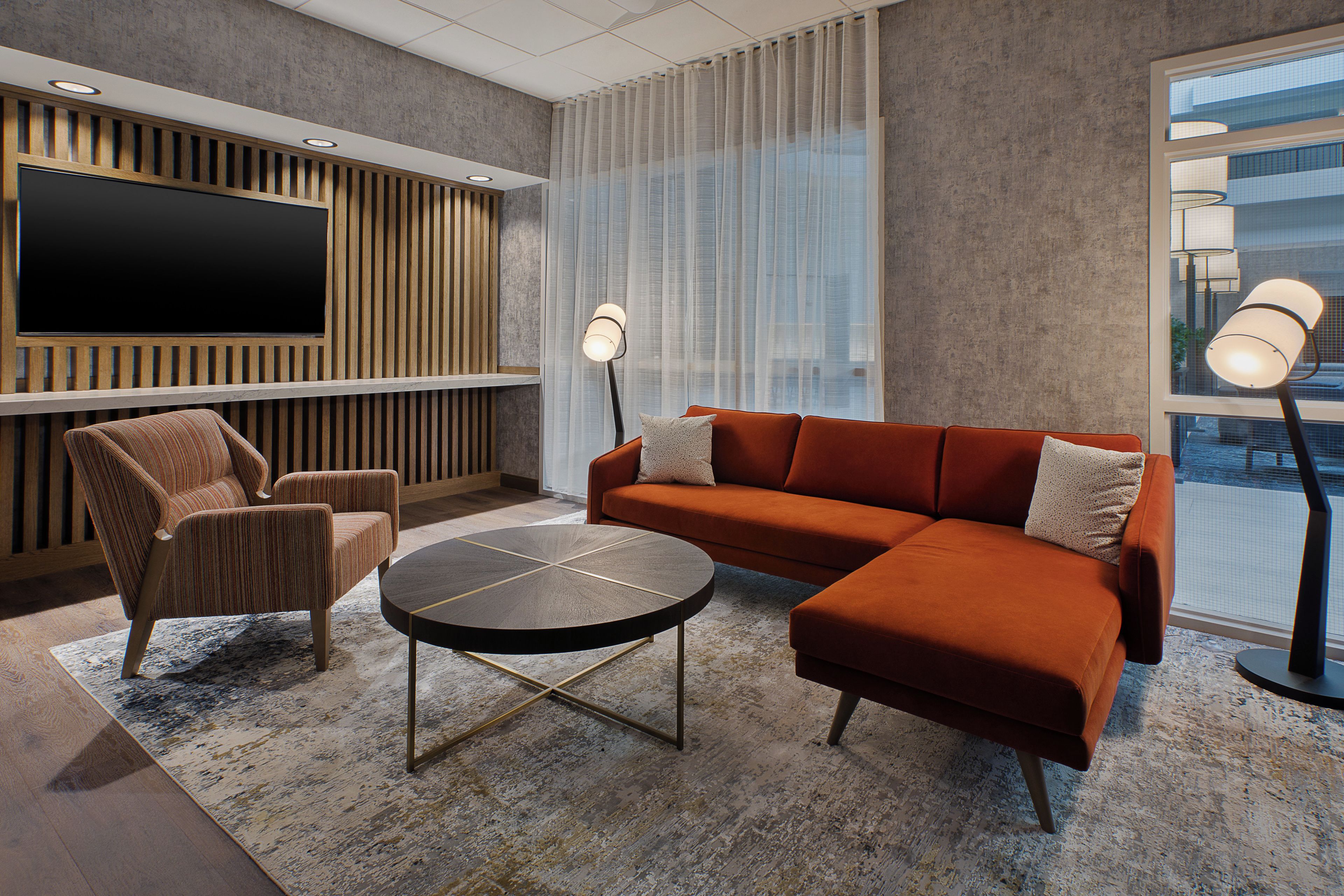 A modern living room with a sectional sofa, a round coffee table, and a flat-screen TV mounted on a wooden panel wall.