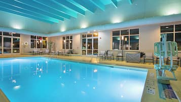 An indoor swimming pool with clear water, surrounded by lounge chairs and a lifeguard stand.
