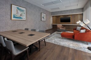 A modern conference room with a wooden table, gray chairs, a large TV, and a red sofa. - Crowne Plaza Bowling Green KY by IHG (Bowling Green)