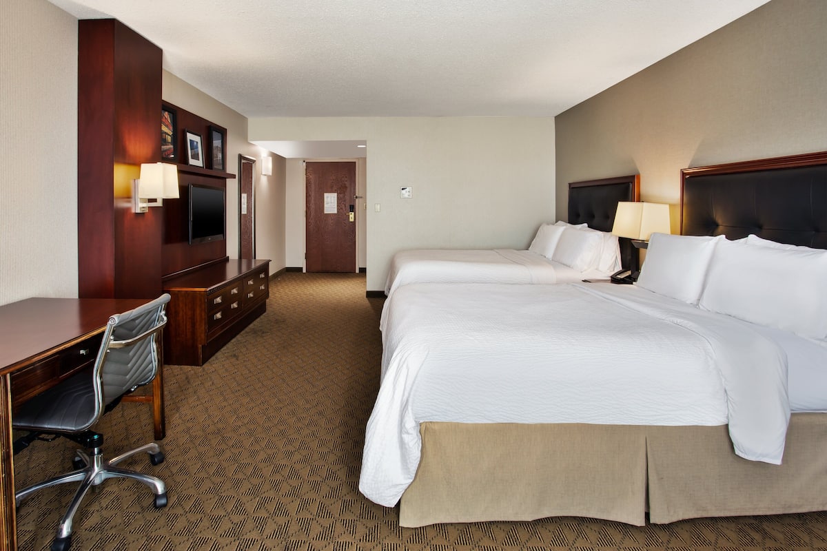 A hotel room with a large bed, a desk with a chair, a TV, and a door leading to another room.