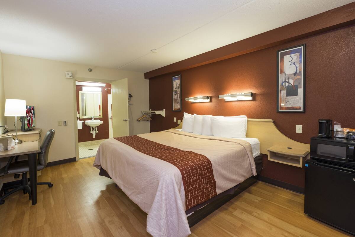 A hotel room with a bed, desk, chair, bedside table, and a coffee machine.