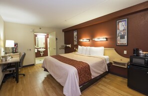A hotel room with a bed, desk, chair, bedside table, and a coffee machine. - Red Roof Inn Cincinnati - Sharonville (Sharonville)