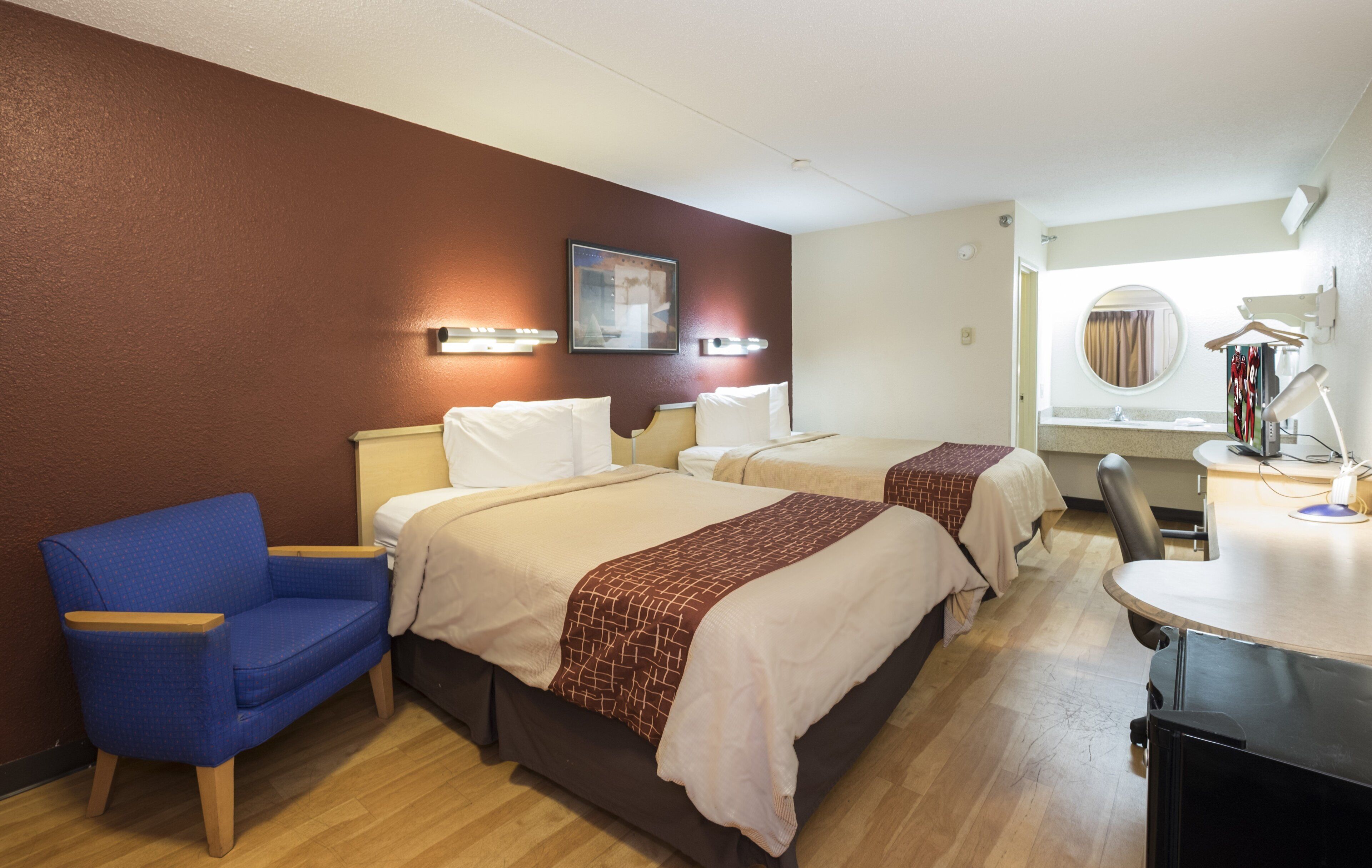 A hotel room with two beds, a desk, a chair, and a mirror.