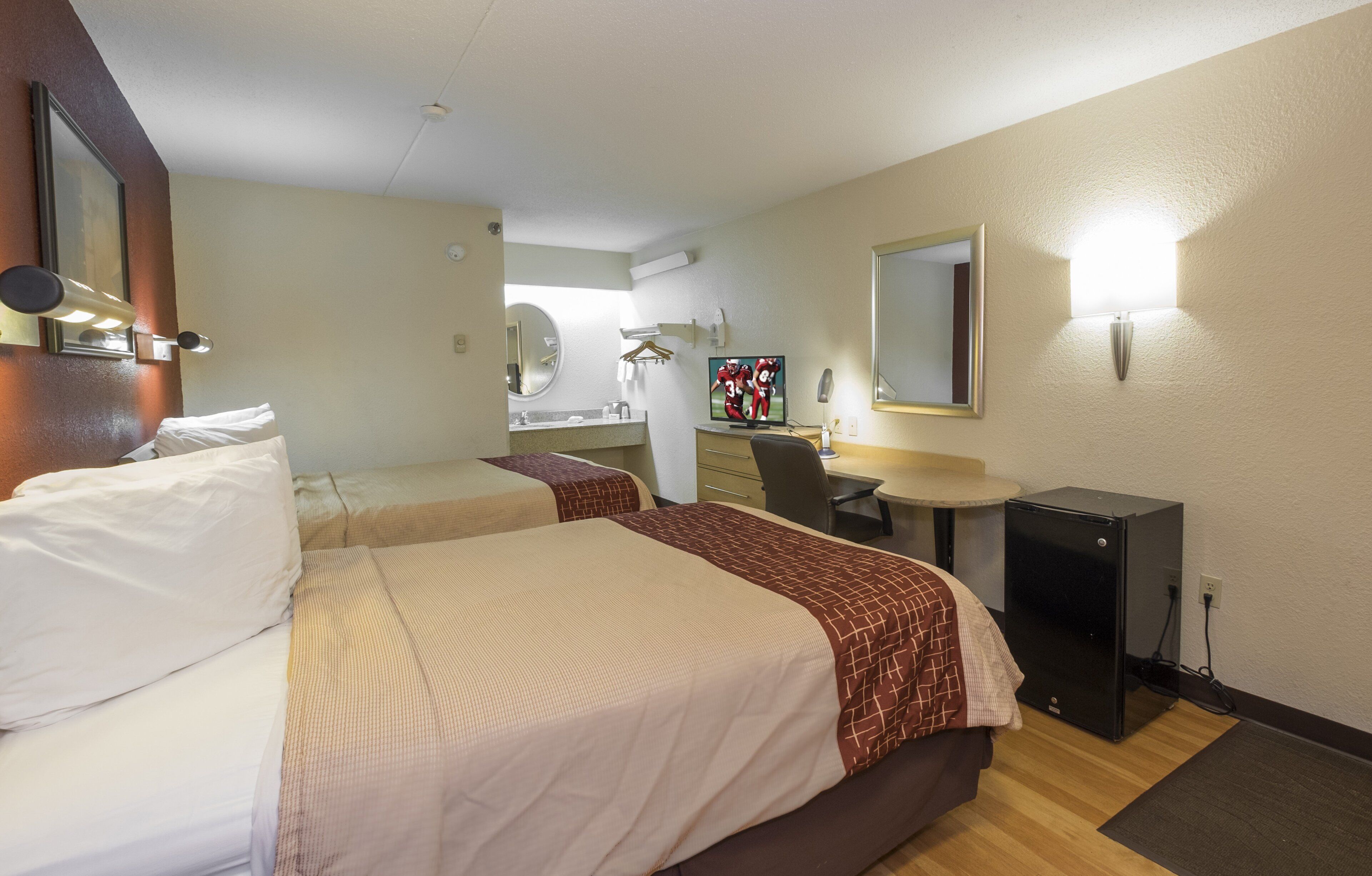 Habitación de hotel con dos camas, un escritorio, un espejo y un televisor.