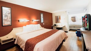 Habitación de hotel con cama, mesitas de noche, un escritorio con silla, televisión y obras de arte en las paredes.