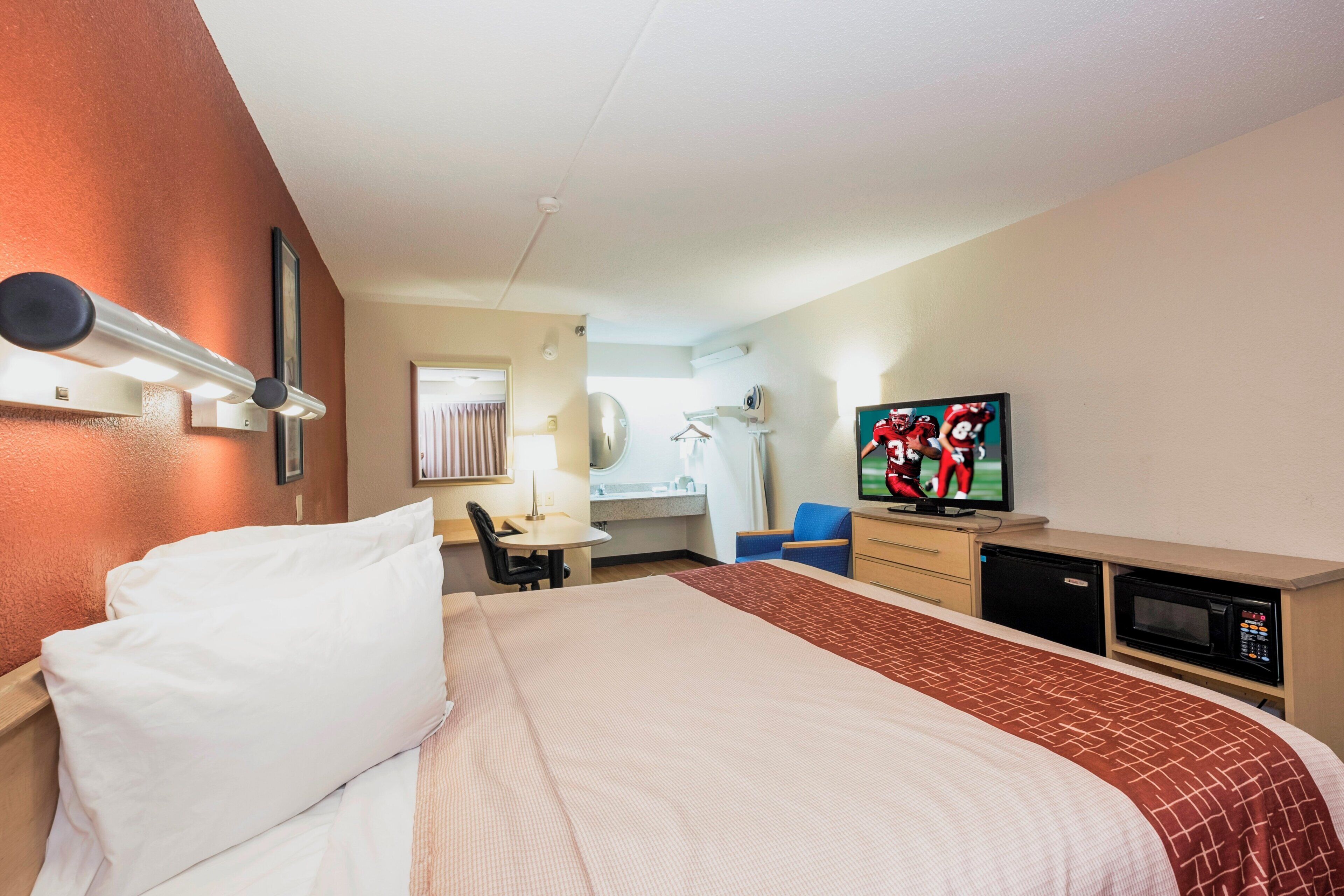 Una habitación de hotel con cama, escritorio, televisión y microondas.