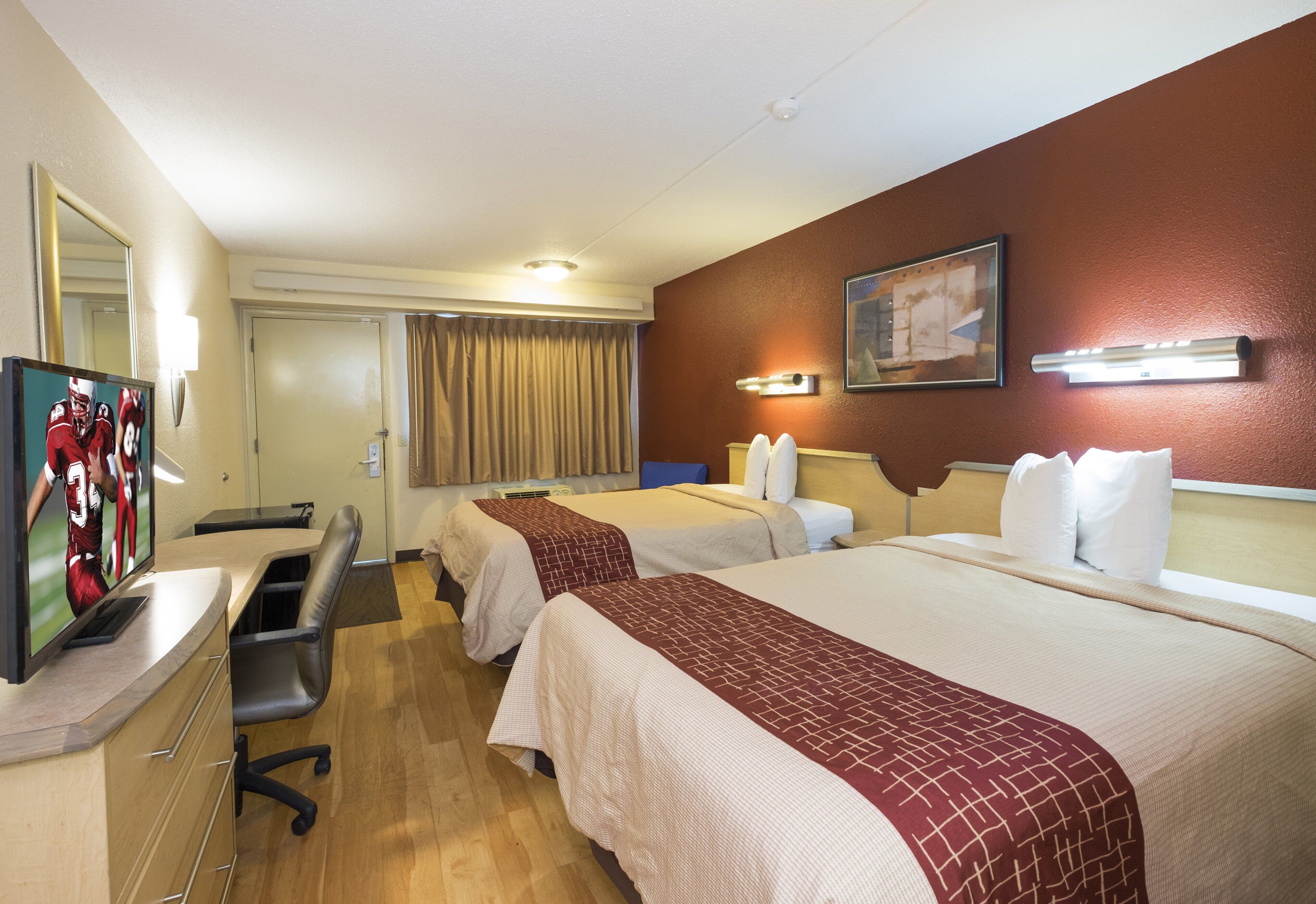 A hotel room with two beds, a desk, a chair, a television, and a painting on the wall.