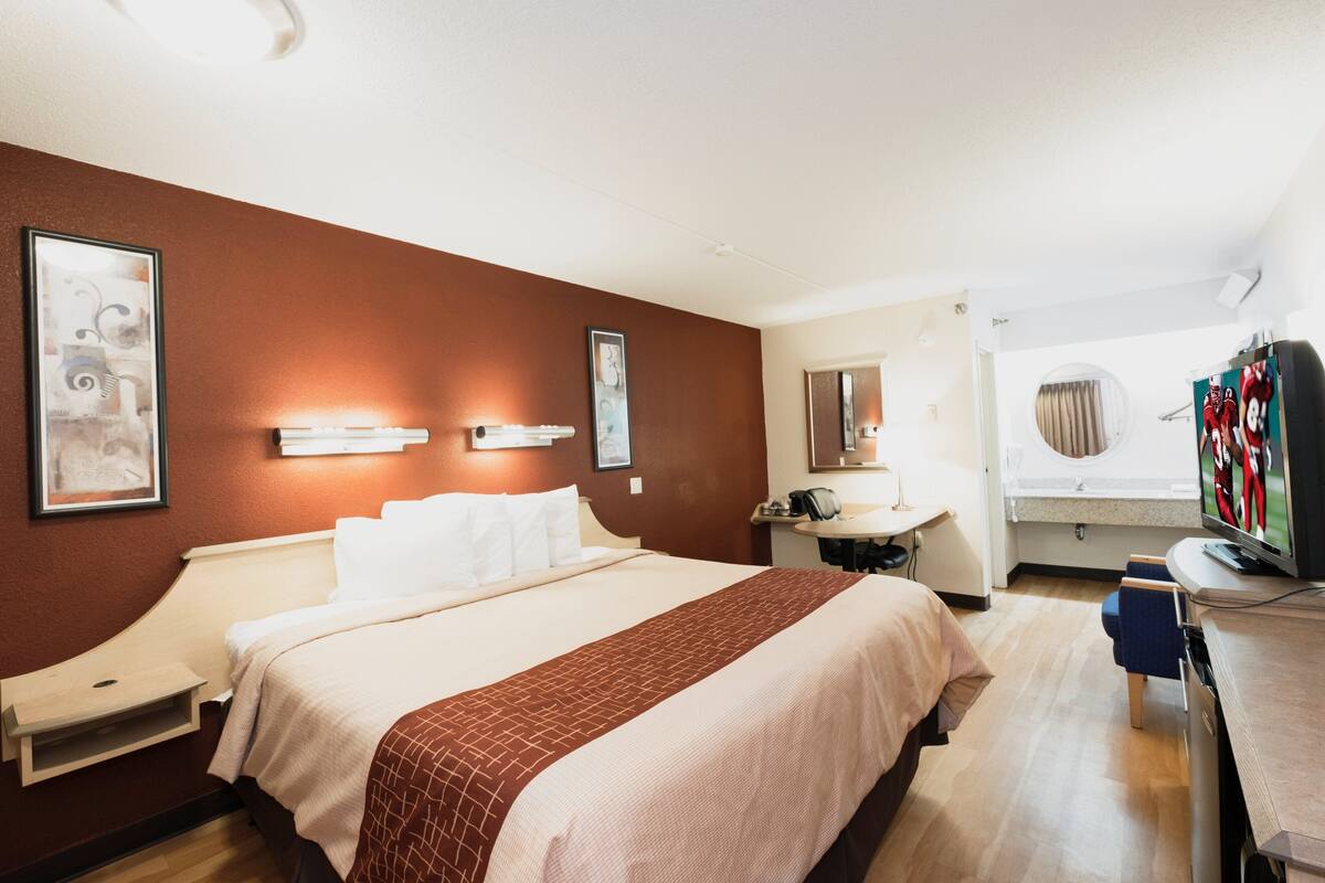 A hotel room with a large bed, bedside tables, a desk with a chair, a television, and artwork on the walls.