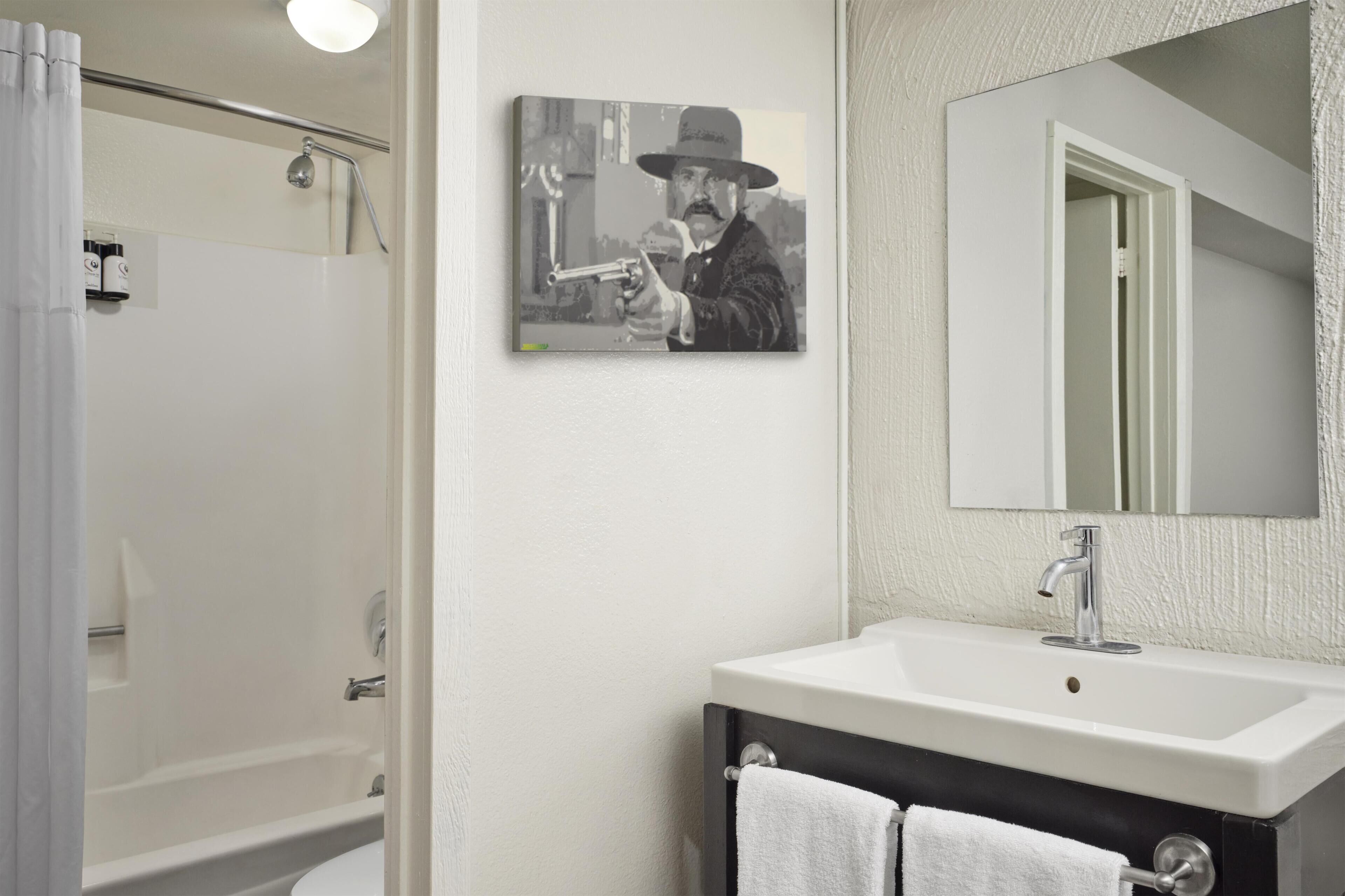 Un bany amb dutxa, un lavabo, un mirall i una fotografia encadrada a la paret.