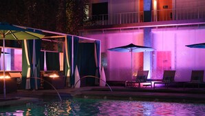 A pool area with lounge chairs and umbrellas, surrounded by a building with a balcony.