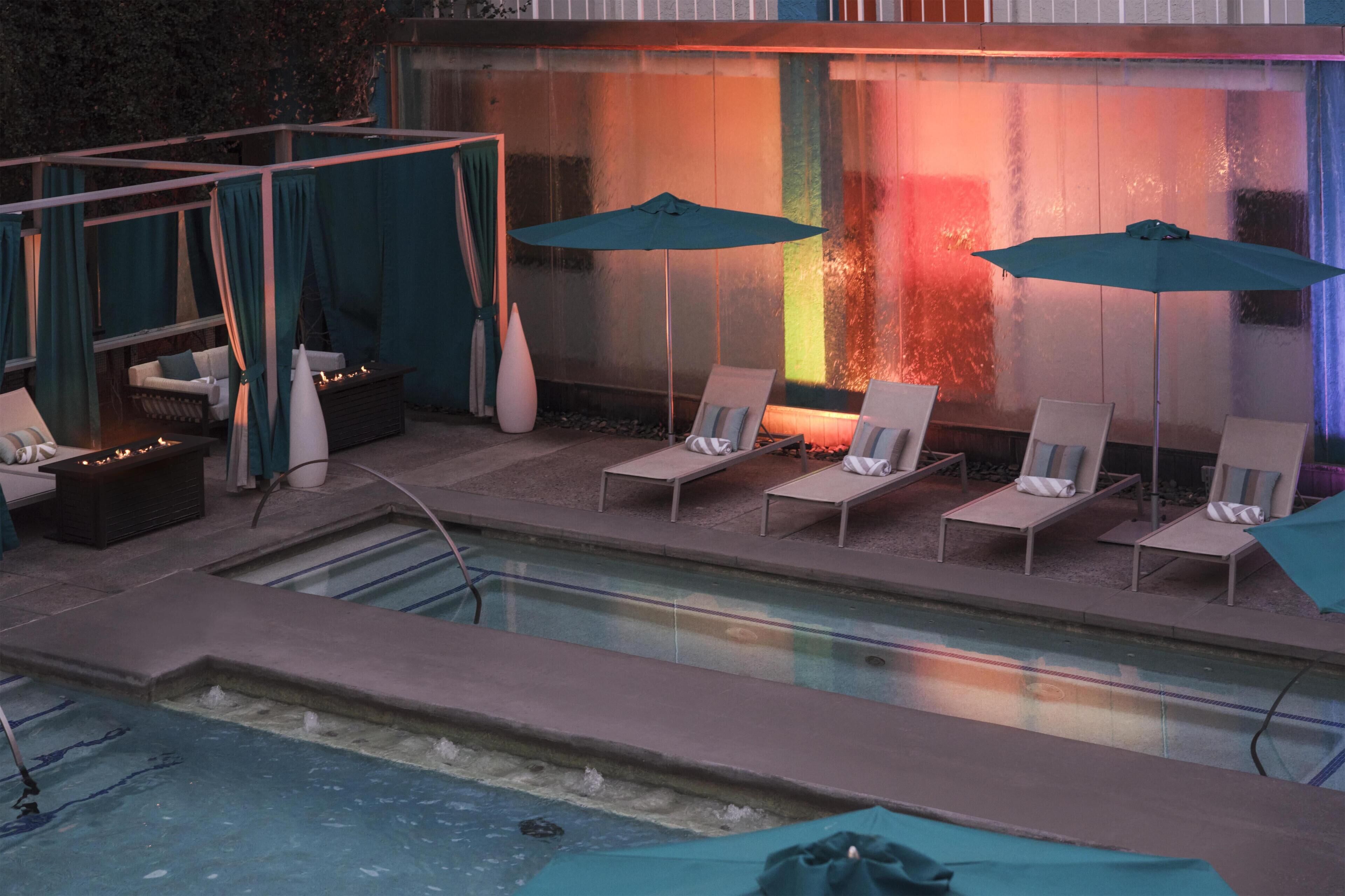 Un espace piscine aménagé avec des chaises longues, des parasols et un élément décoratif aquatique.