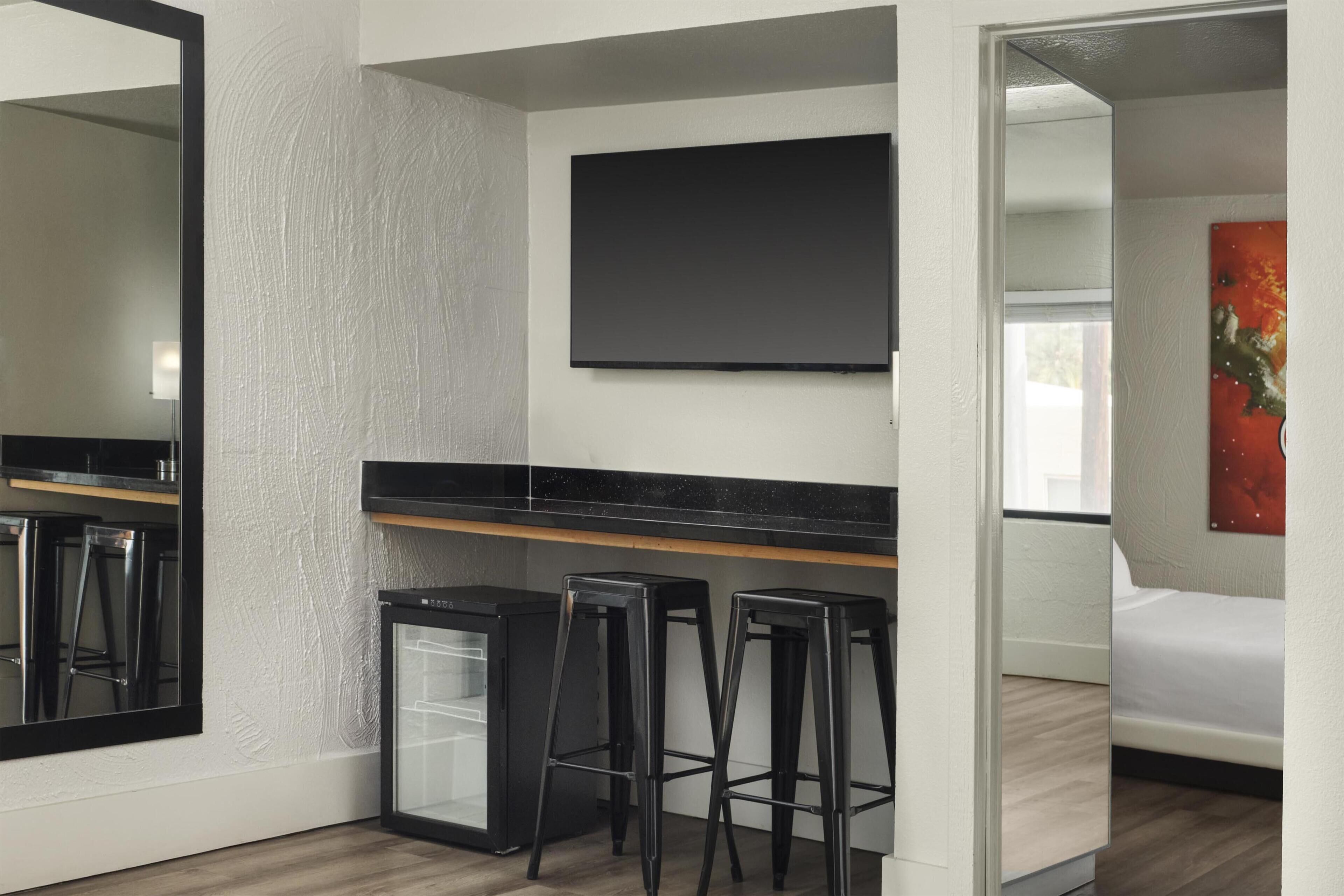 A modern room with a flat-screen TV, a small refrigerator, and two bar stools.