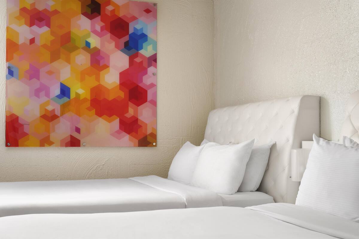 A hotel room with a bed, pillows, and a colorful abstract painting on the wall.