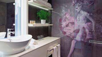 A modern bathroom with a large white sink, a glass shower enclosure, and a decorative mural.