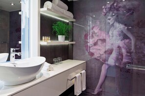 A modern bathroom with a large white sink, a glass shower enclosure, and a decorative mural.