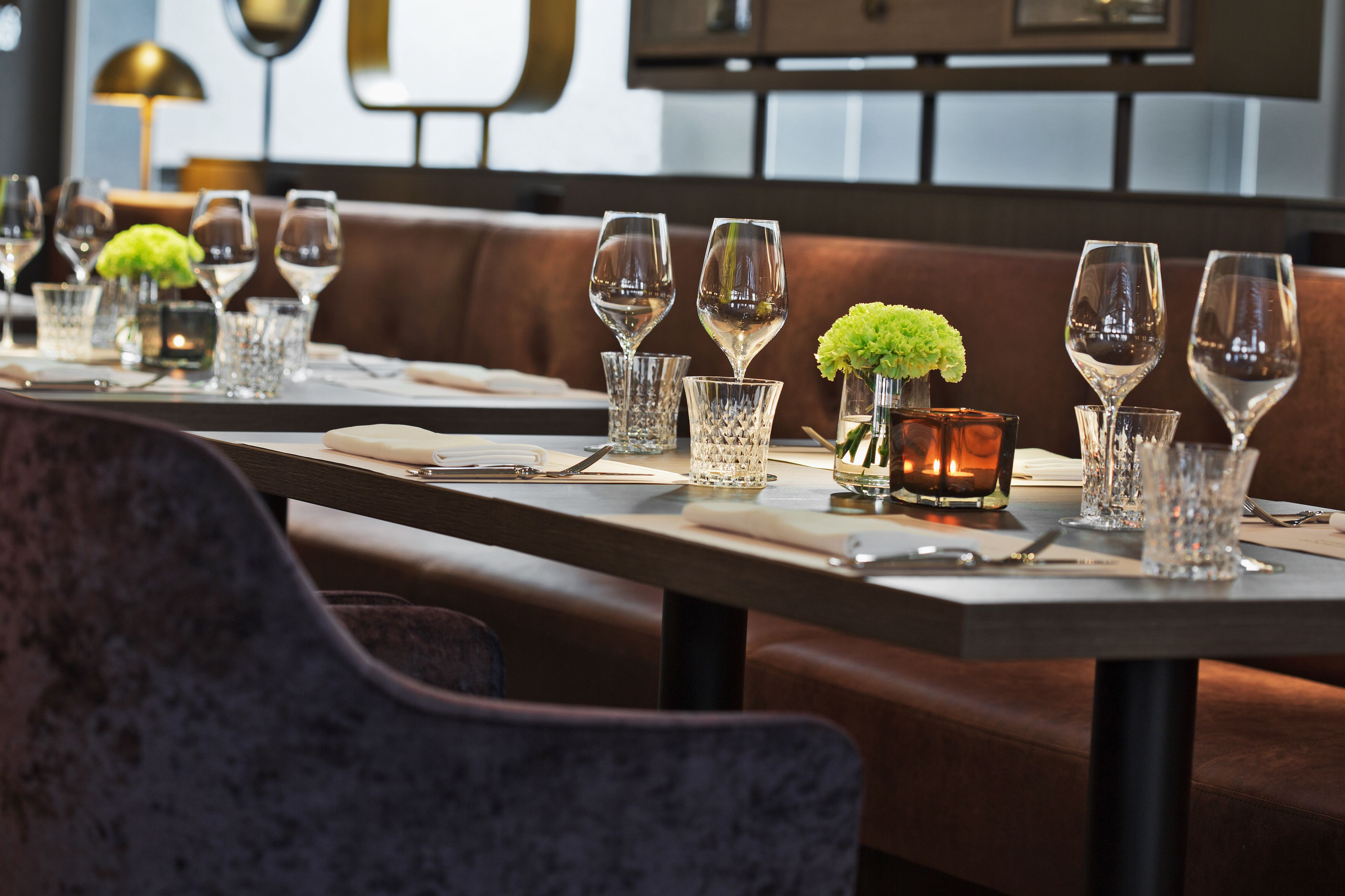 A restaurant setting with tables set for dining, featuring glassware and small floral centerpieces.
