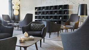 Un saló modern amb butaques grises fosques, una taula de centre amb llibres i un objecte decoratiu, un prestatge negre amb diversos objectes i una lampada de terra negra gran.