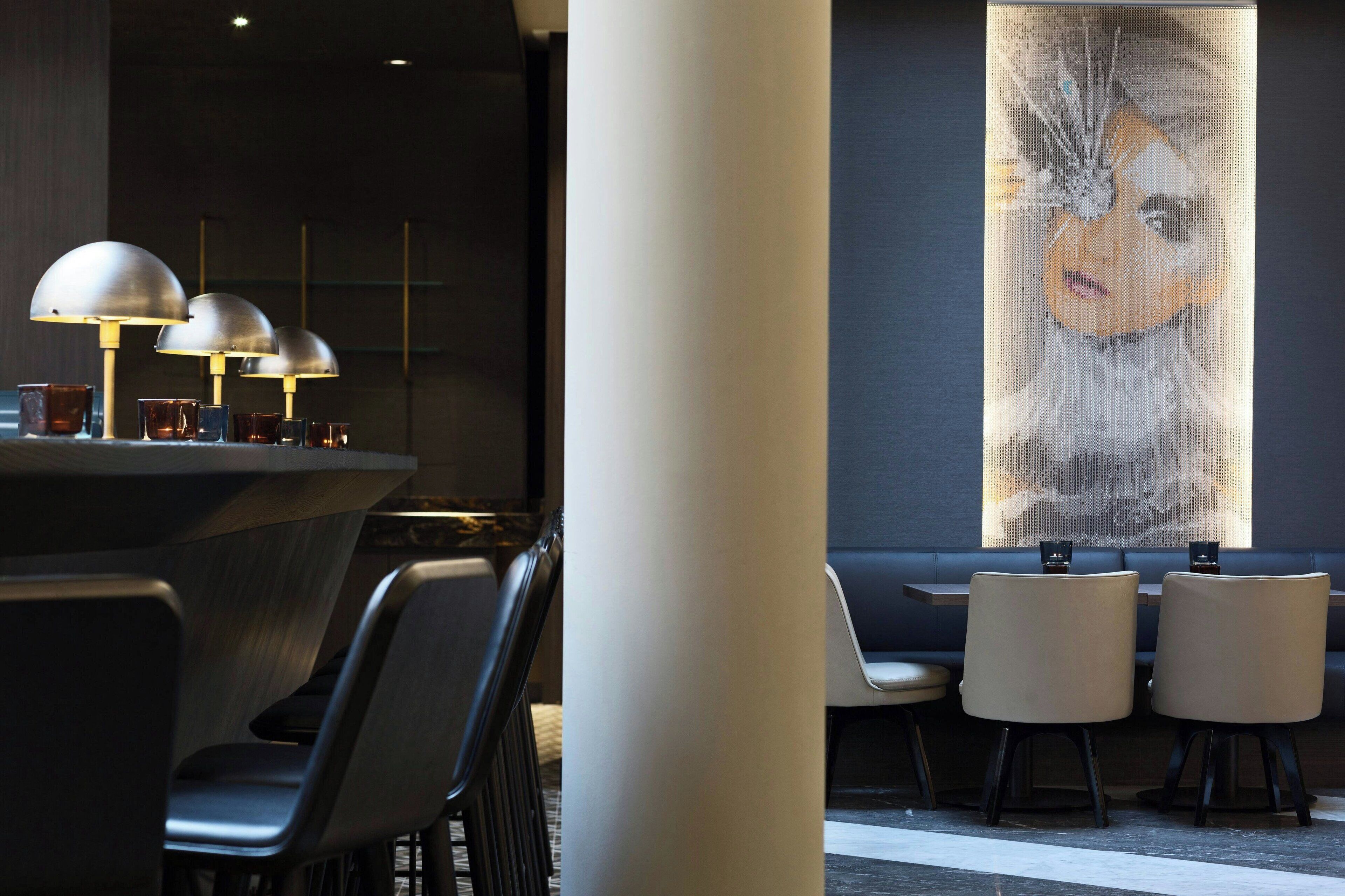 Un interior moderno con una zona de bar que presenta tres lámparas y un cuadro abstracto grande en la pared.