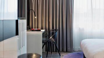 Una habitación de hotel moderna con cama, escritorio con silla, televisión y ventana con cortinas.