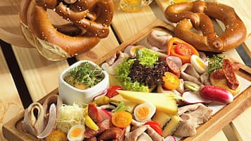 A wooden table with pretzels, a charcuterie board with meats, cheese, and vegetables, and beer mugs.