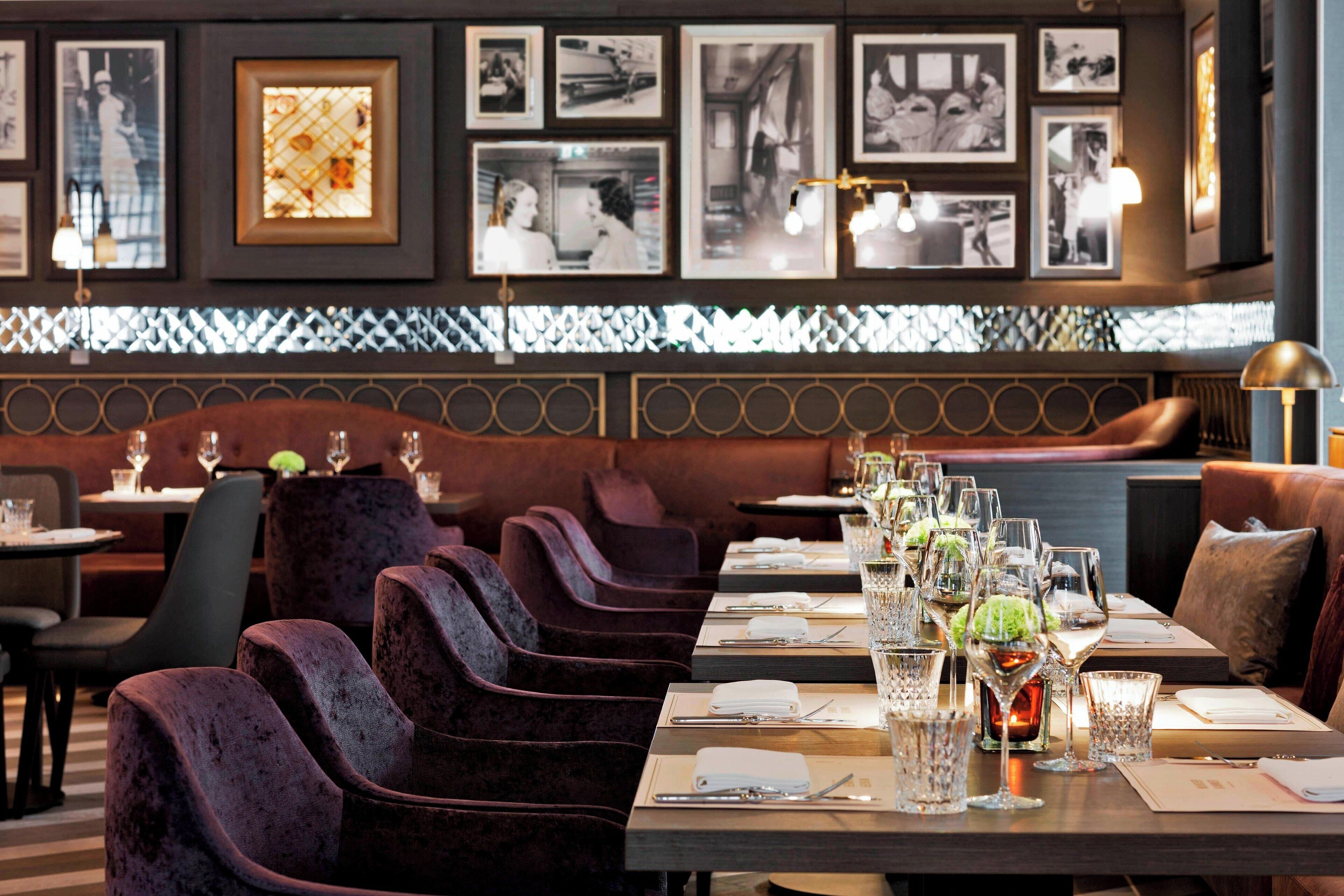 A restaurant with velvet chairs, tables set with wine glasses and menus, and framed pictures on the wall.