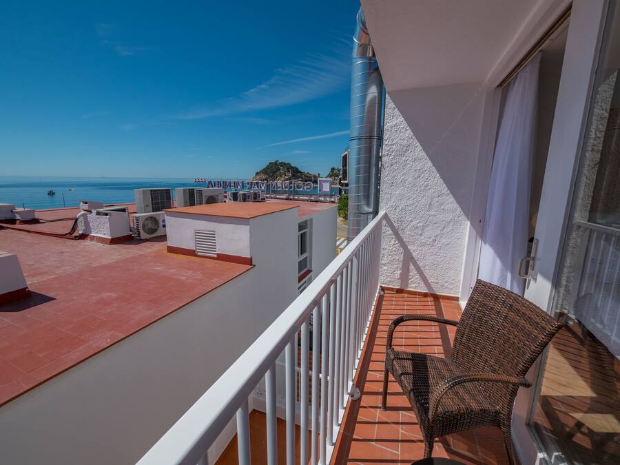 Un balcón con una silla de mimbre, equipos de aire acondicionado y vista al mar.