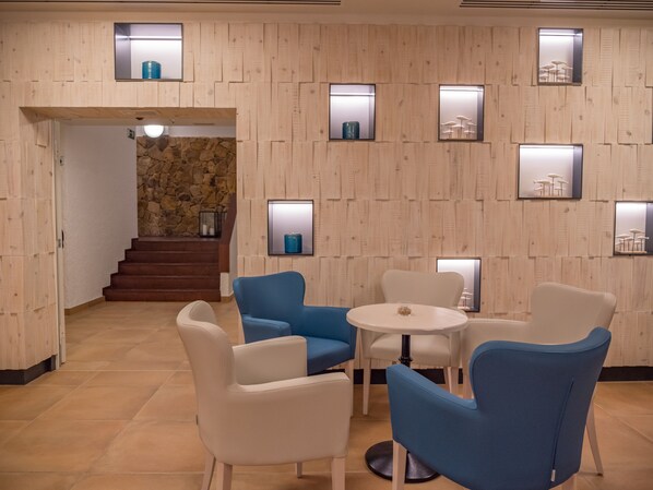 A modern interior with a stone wall, wooden panel walls, and a staircase leading to a higher level. There are several chairs and a table in the foreground. - Golden Mar Menuda (Tossa de Mar)