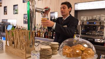 Un barista en train de verser une boisson dans un verre, un présentoir de croissants et un robinet à bière.