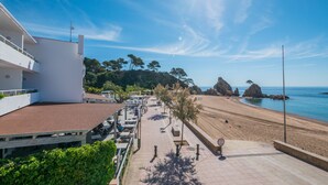 A coastal hotel with a paved walkway leading to a beach, featuring a view of the sea and rocky formations. - Golden Mar Menuda (Tossa de Mar)