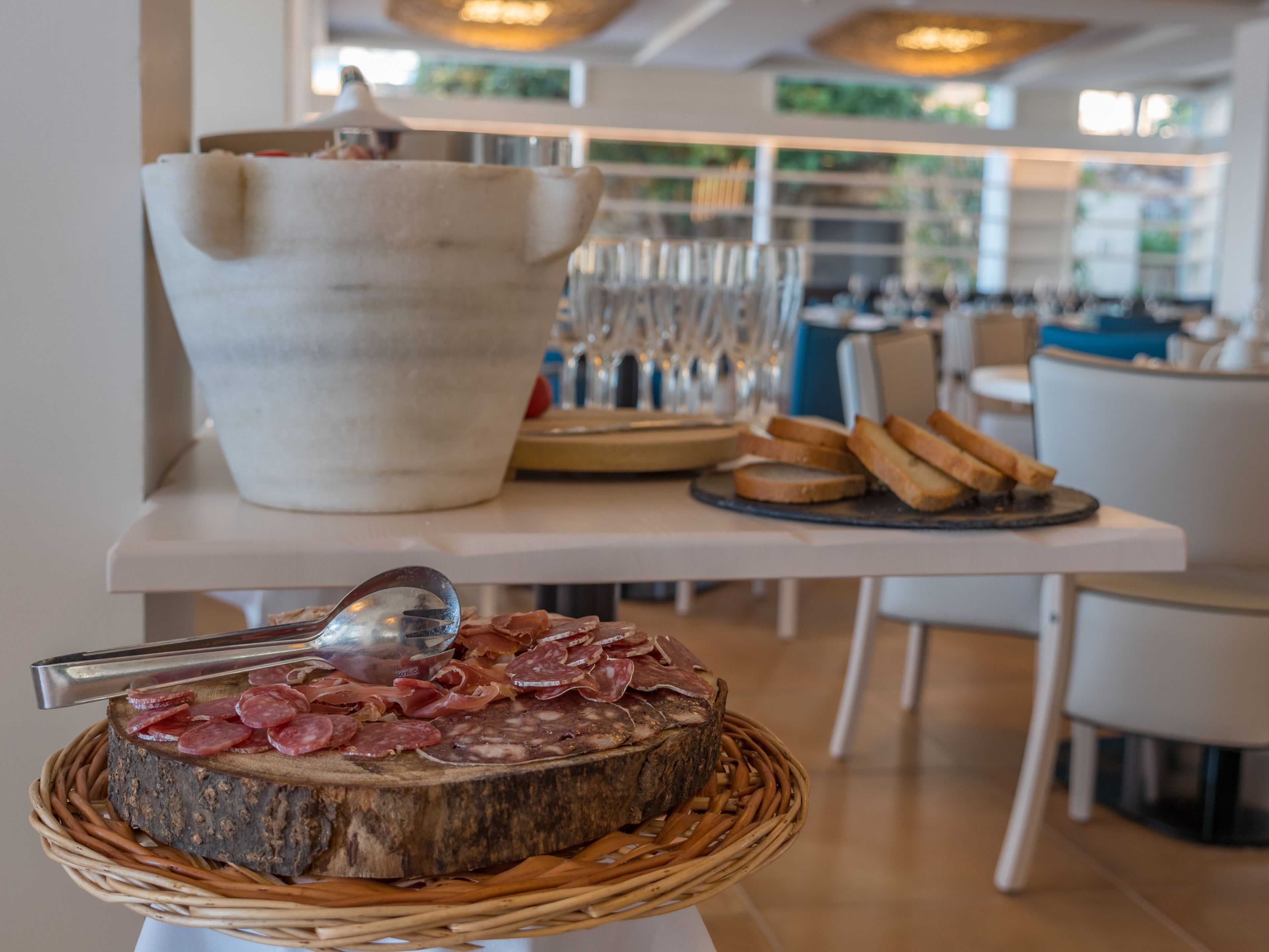 A dining table with a wooden platter of cured meats, a large ceramic pitcher, and a glass set.