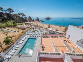 Uma área de piscina no terraço com espreguiçadeiras, piscina e vista para a praia e o mar.