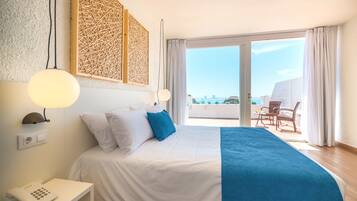 Habitación de hotel con cama, teléfono en la mesita de noche, un panel decorativo en la pared y vista al mar a través de una puerta corrediza de cristal.