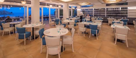 Un restaurante con varias mesas y sillas, amplias ventanas y vistas al mar.