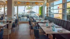 A restaurant with tables set for dining, large windows offering a view of the sea, and a seating area with a view of the ocean. - Golden Mar Menuda (Tossa de Mar)