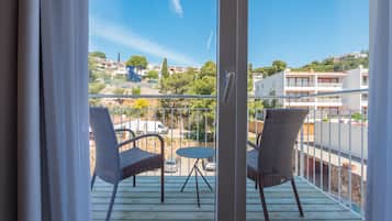 A balcony with wicker chairs and a small table, overlooking a residential area with buildings and greenery.