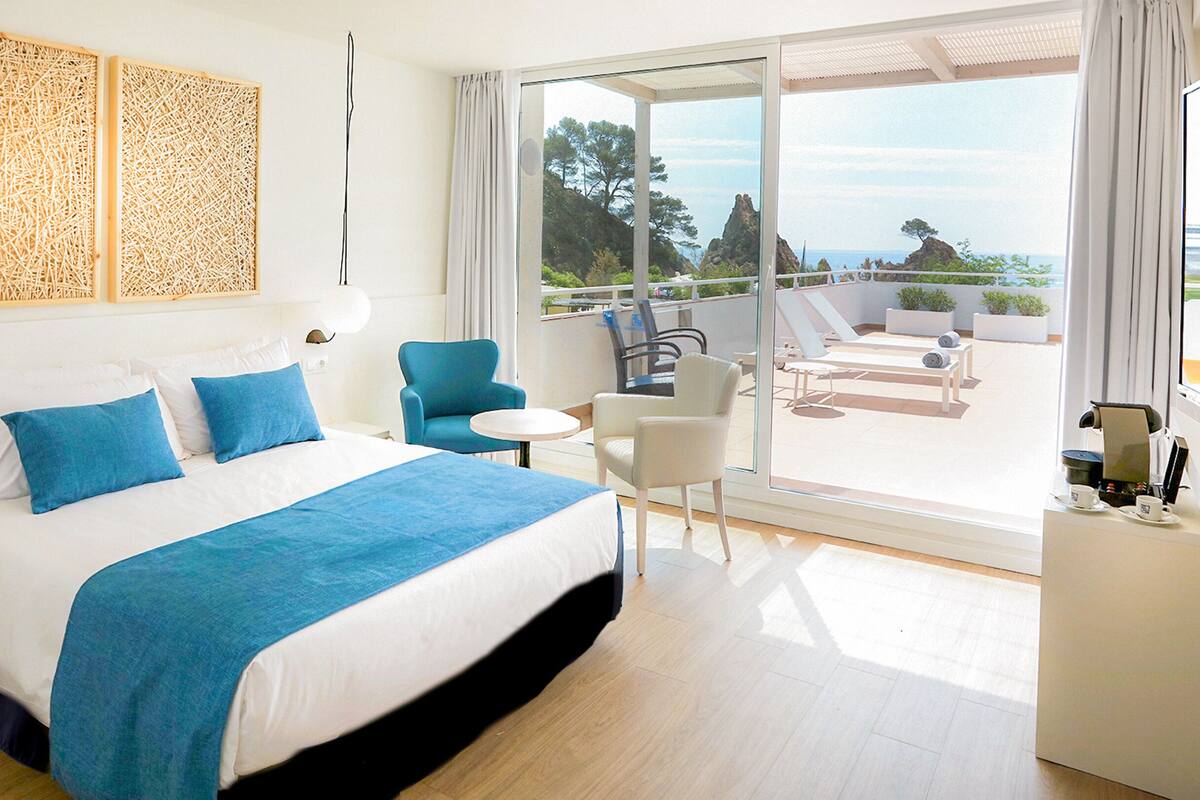 A hotel room with a large bed, a balcony with seating, and a view of the sea.