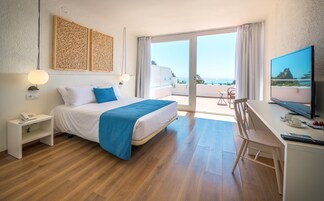 Quarto de hotel com cama, escrivaninha, televisão e varanda com vista para o mar.