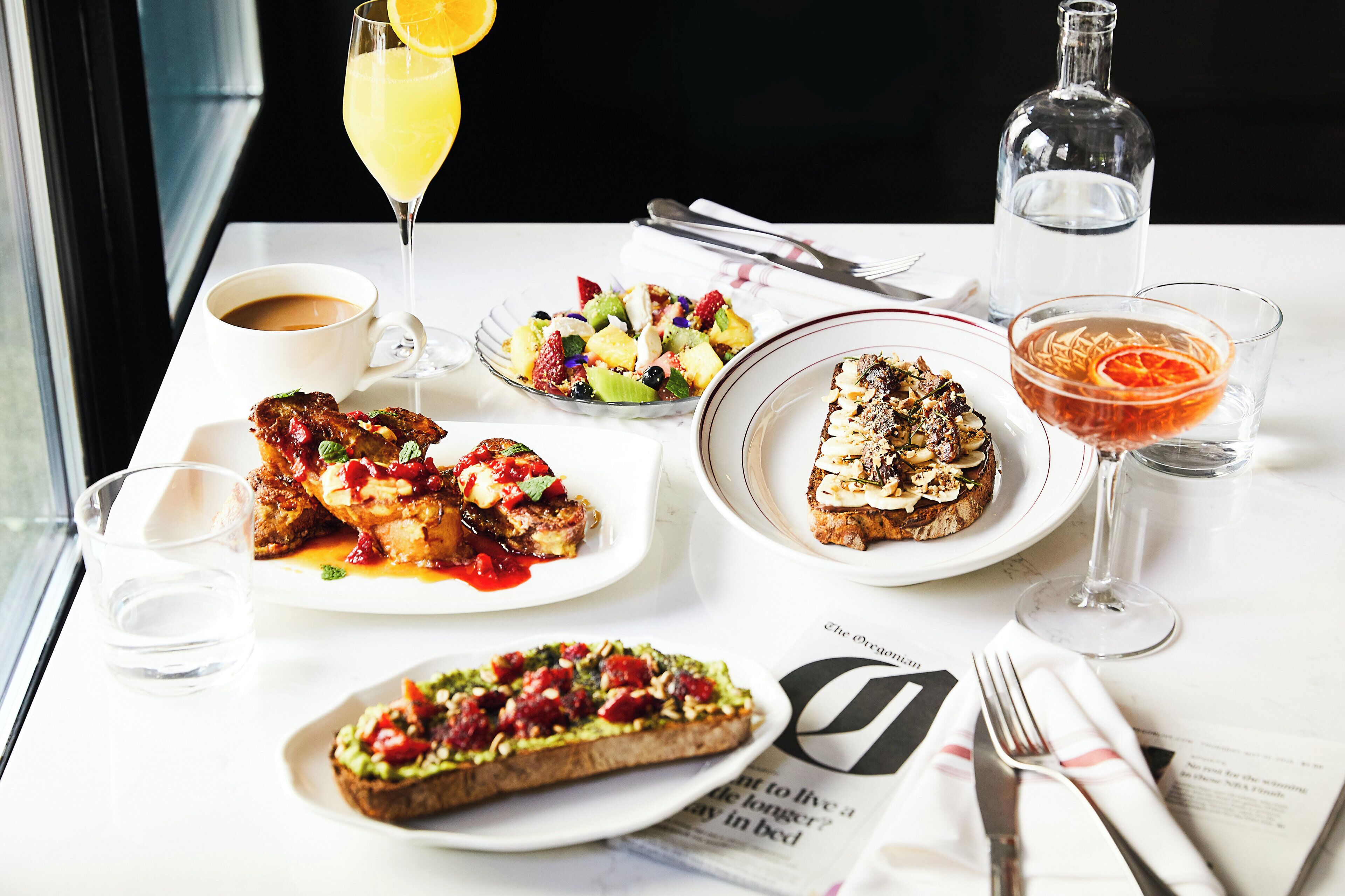 A table set with various dishes, a glass of orange juice, a bottle of water, and a newspaper.