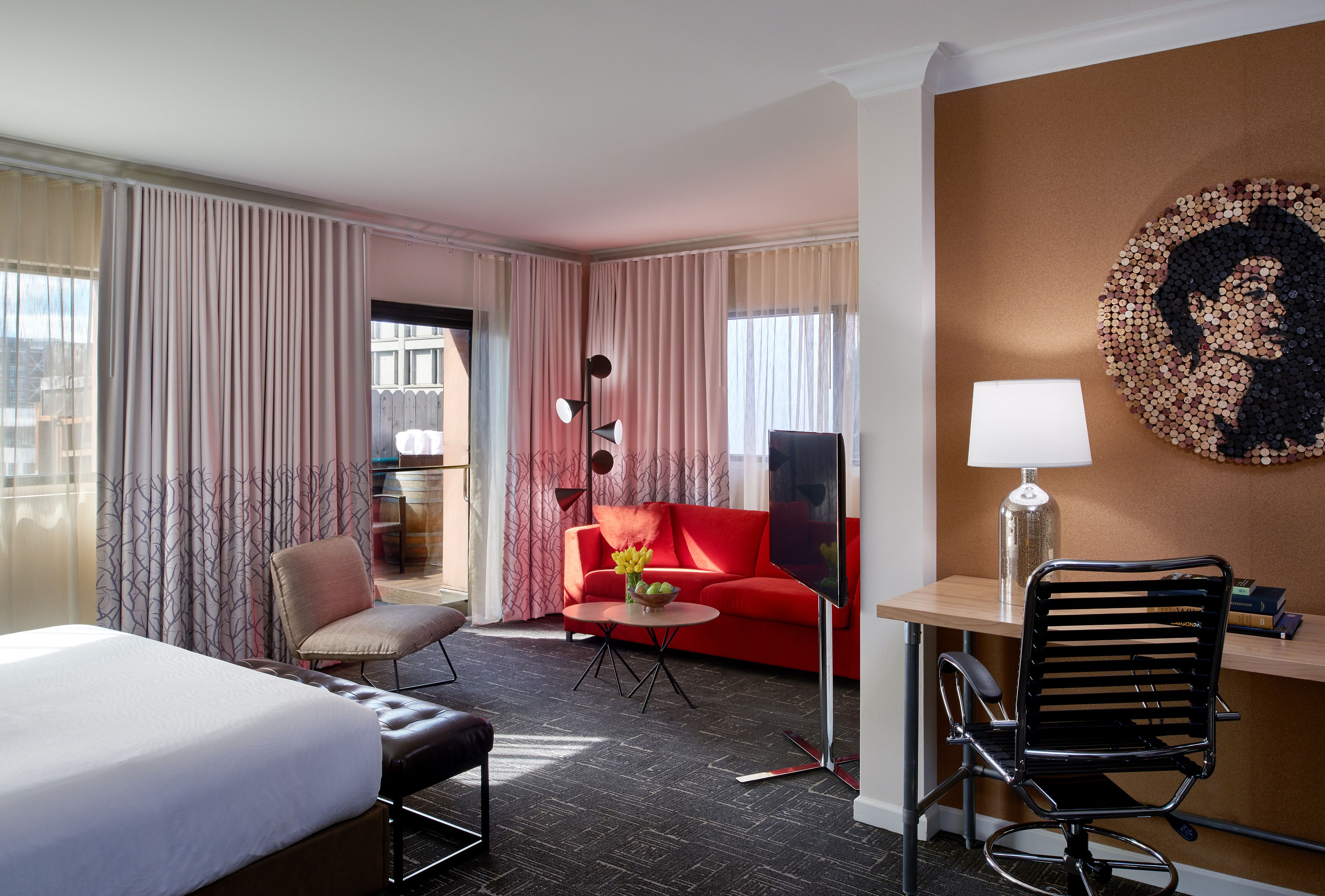 Habitación de hotel con cama, escritorio, sofá rojo, silla y ventana grande con cortinas.
