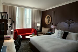 A hotel room with a large bed, a red sofa, a desk with a lamp, and a view of the outdoors through the window. - Kimpton Hotel Vintage Portland by IHG (Portland)