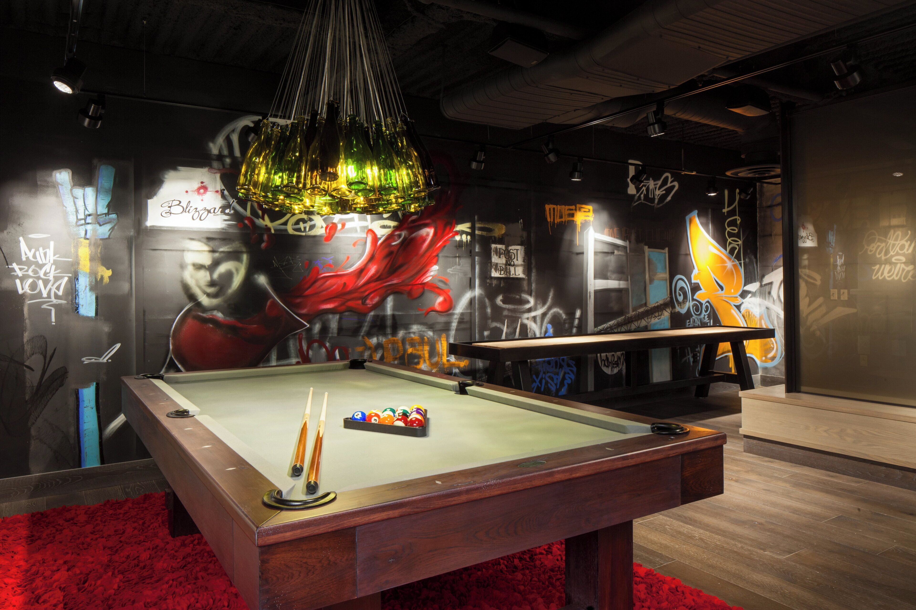 A pool table with a cue stick and balls, surrounded by graffiti and a mural.